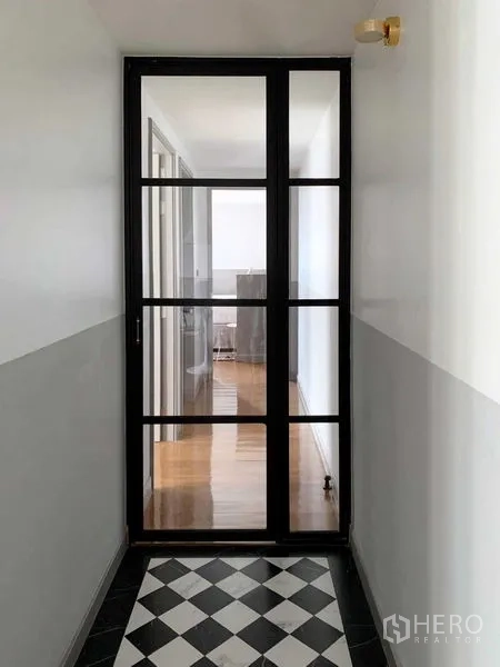Condominium for sale in Watthana, Bangkok - Narrow corridor ending at a black-framed glass door with black-and-white tiled floor.