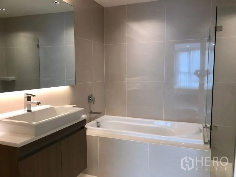 Condominium for sale in Khlong Toei, Bangkok - Contemporary bathroom with bathtub, glass screen and wide vanity mirror.