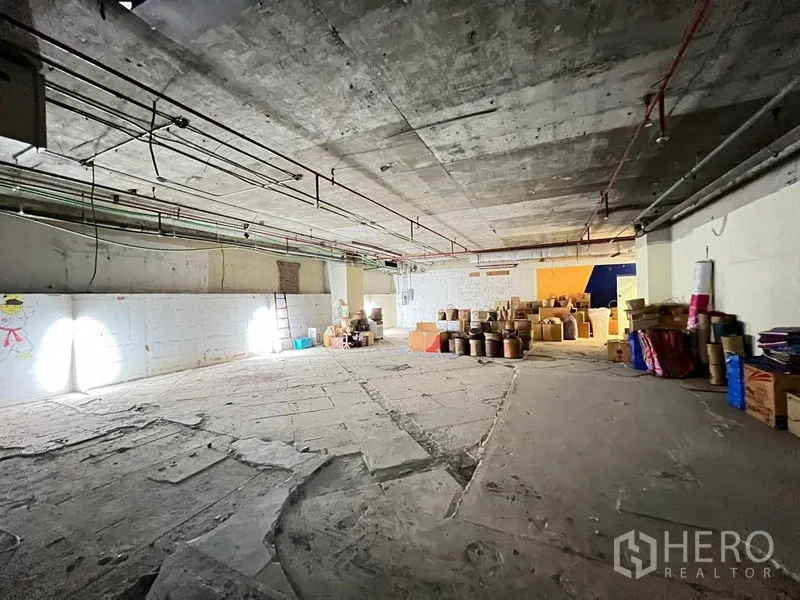 Retail Space for rent - Open-plan retail shell with rough concrete floor, bright wall lights and stacked packaging.