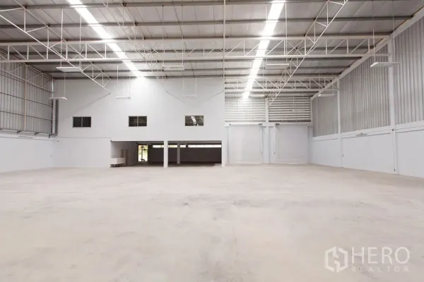Factory for rent in Si Racha, Chon Buri - High-ceiling warehouse interior with mezzanine offices and two large roller doors.