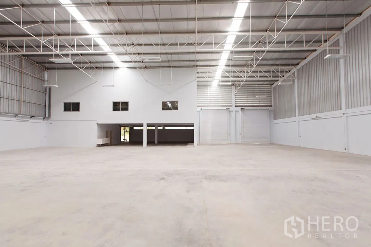 Factory for rent in Si Racha, Chon Buri - High-ceiling warehouse interior with mezzanine offices and two large roller doors.