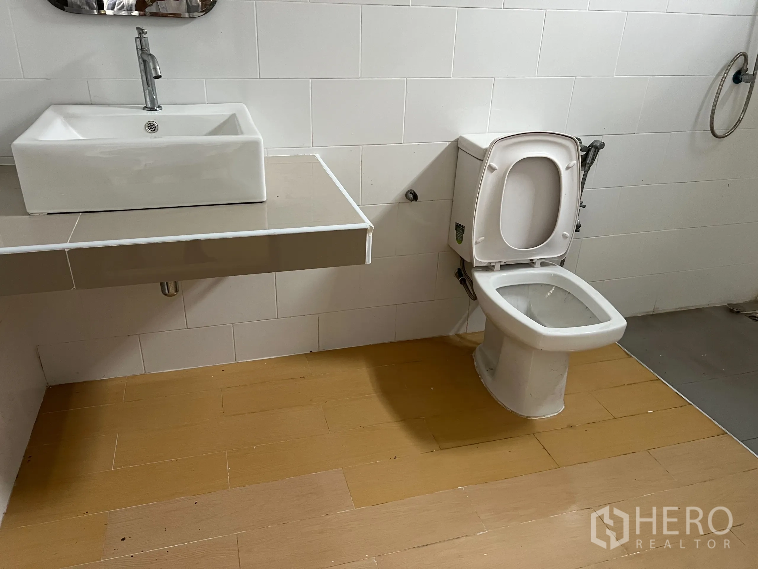 Warehouse for sale in Bang Len, Nakhon Pathom - Close-up of toilet and sink in a white-tiled restroom with handheld bidet.
