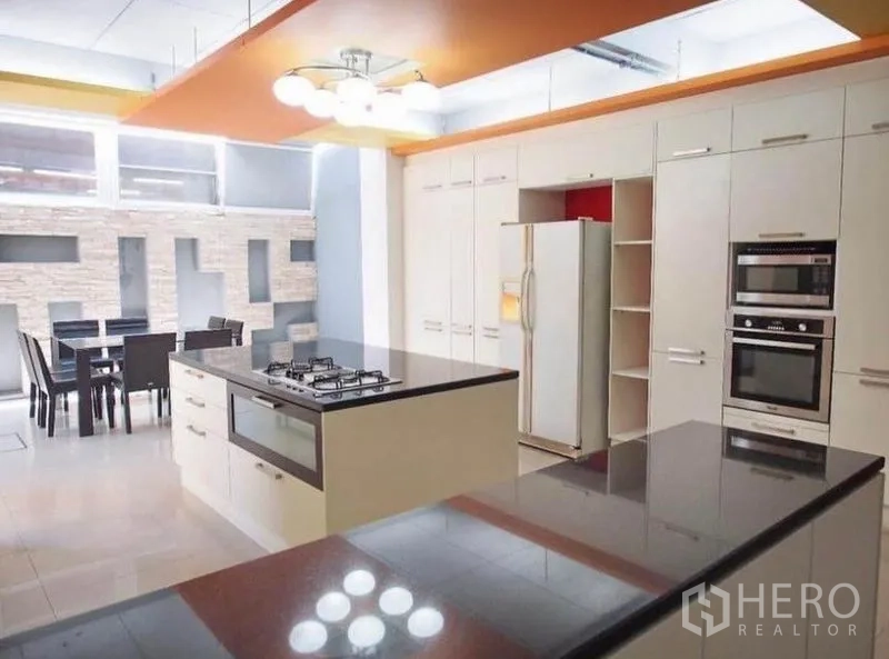 联排别墅 出租在Wang Thonglang, Bangkok - 现代厨房，岛台燃气灶，黑色石面台，嵌入式烤箱与用餐角。