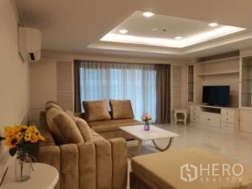 Apartment for rent in Watthana, Bangkok - Living room with TV console and shelving unit, sofa set and large curtained window.