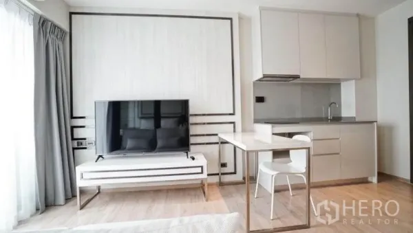 Condominium for sale in Khlong Toei, Bangkok - Minimalist kitchenette with upper cabinets, cooktop, sink and a TV console with flatscreen.
