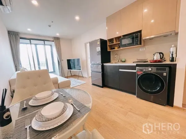 Condominium for rent in Ratchathewi, Bangkok - Bright open‑plan living room with kitchenette, dining set and balcony doors.