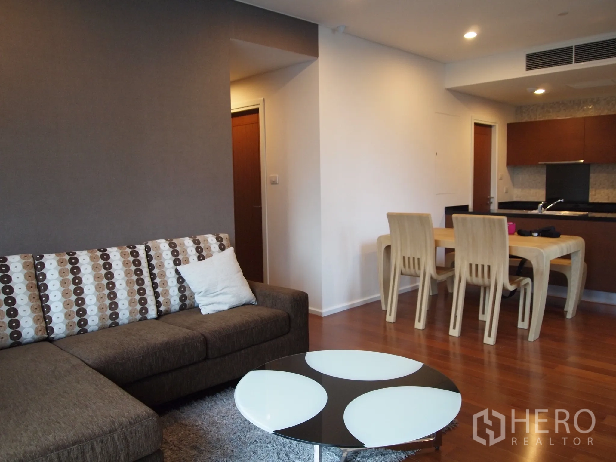 Condominium for rent or sale in Watthana, Bangkok - Open-plan living area with L-shaped sofa, dining table and kitchen backdrop.