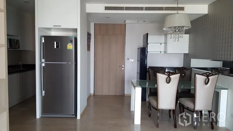 Condominium for rent in Khlong Toei, Bangkok - Open-plan dining and pantry with stainless refrigerator, glass-top table and wood entrance door.