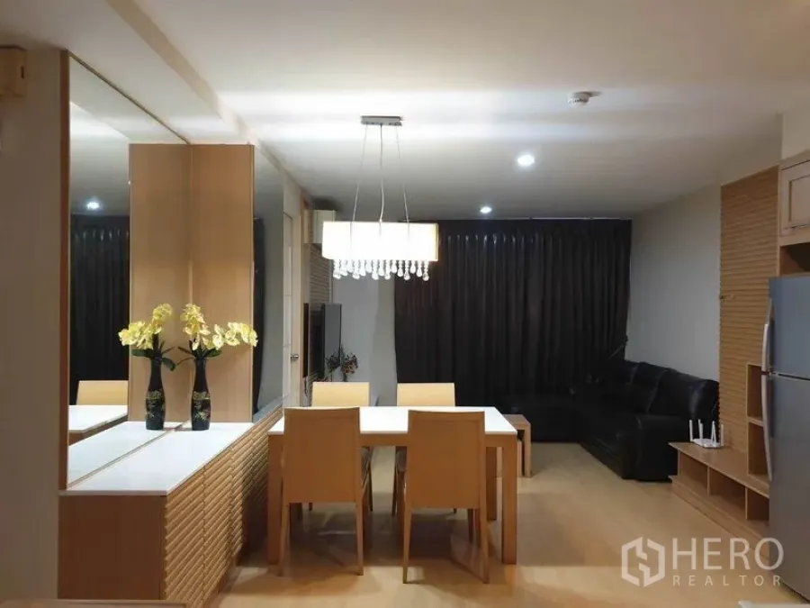 公寓 出租在Watthana, Bangkok - 餐区四人餐桌搭配水晶吊灯与镜面储物台，旁接皮沙发客厅。