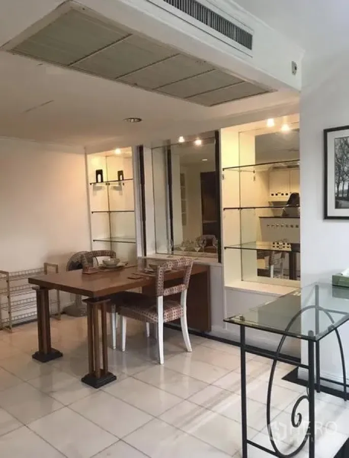 Condominium for rent in Khlong Toei, Bangkok - Bright dining corner with wooden table, rattan chairs and glass display shelves beside a pass-through to the kitchen.