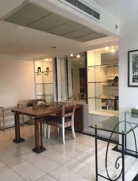 Condominium for rent in Khlong Toei, Bangkok - Bright dining corner with wooden table, rattan chairs and glass display shelves beside a pass-through to the kitchen.