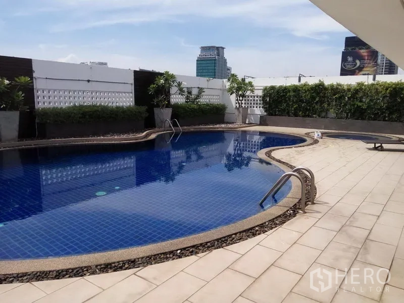 公寓 出租或出售在Pathum Wan, Bangkok - 户外游泳池，蓝色池砖与日光平台，背景为曼谷天际线。