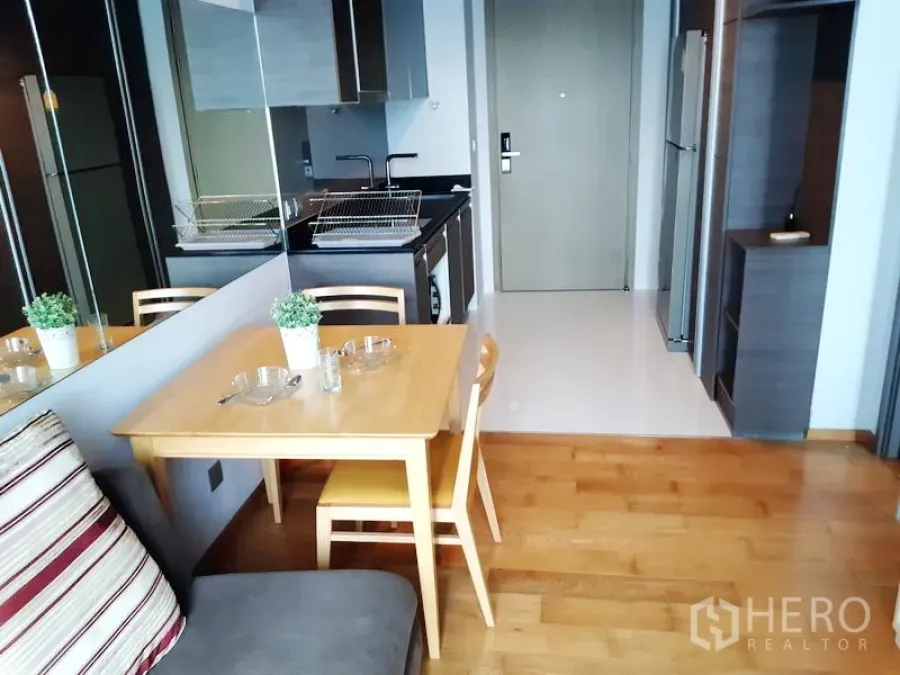 Condominium for rent in Khlong Toei, Bangkok - Compact dining nook beside a mirrored wall and modern built-in kitchen with appliances.
