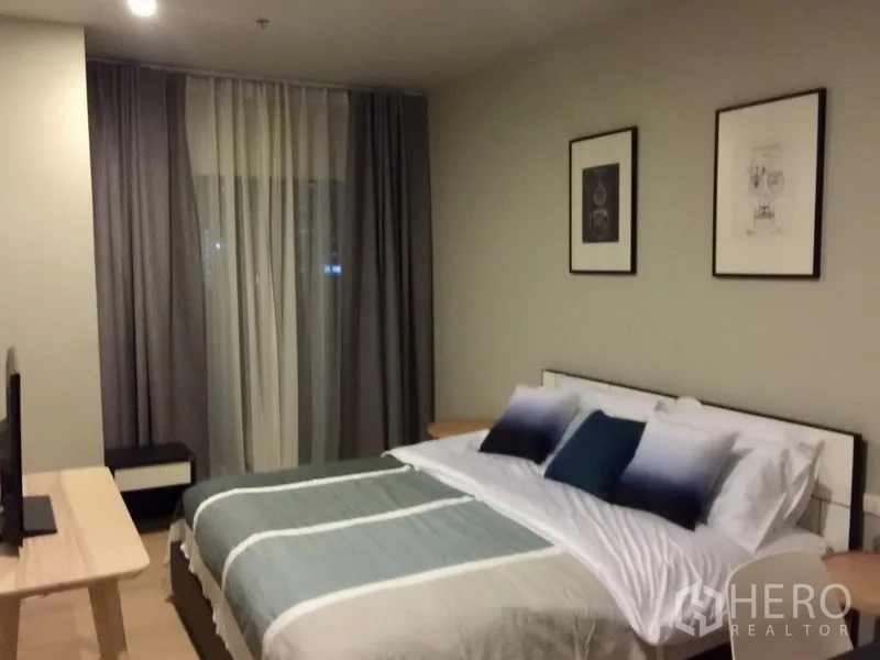Condominium for rent in Bangkok - Bedroom with neatly made queen bed, framed artwork, side tables and layered curtains in a Khlong Toei condo.