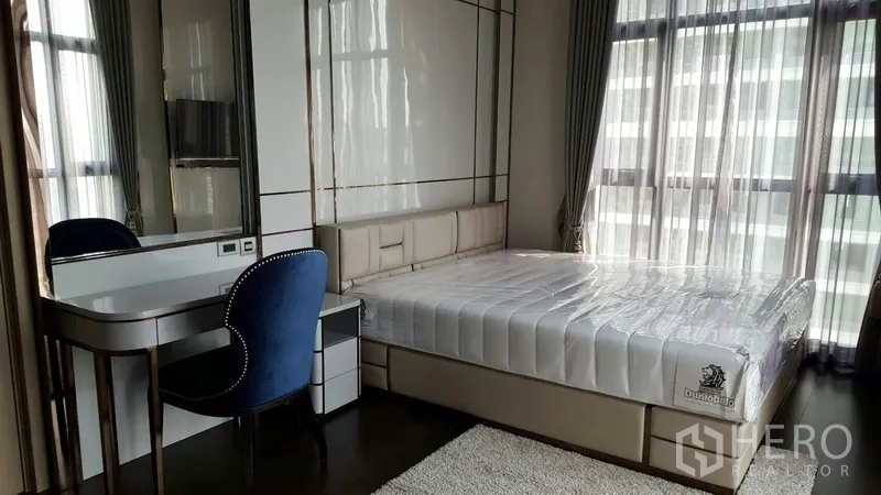 Condominium for rent in Watthana, Bangkok - Bedroom with a large bed, vanity desk and full-height windows with sheer curtains.