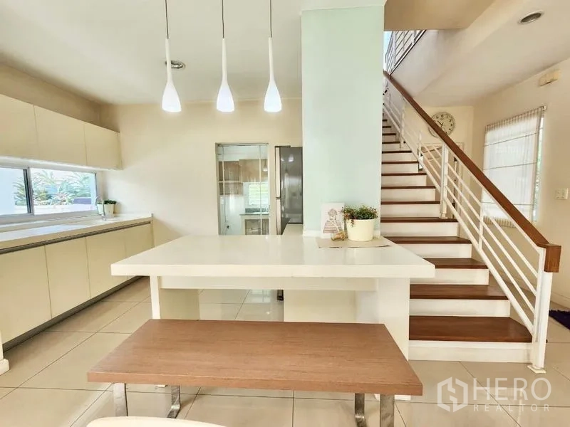独立式住宅 出租在Prawet, Bangkok - 开放式餐区与岛台，吊灯和楼梯相连，通向厨房。