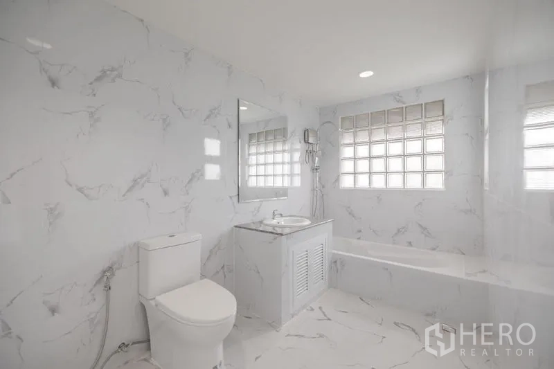 Townhouse for sale - All-white marble bathroom with bathtub, vanity and glass-block window.