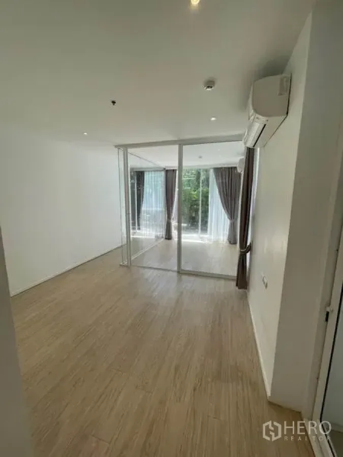 Home Office for rent in Khlong Toei, Bangkok - Bright home office room with glass partition, light wood flooring, floor-to-ceiling windows, curtains and wall-mounted air conditioner overlooking greenery.