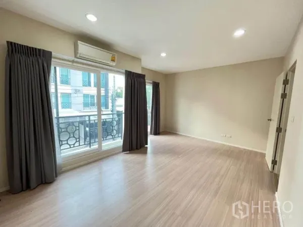 Townhouse for sale in Bang Kapi, Bangkok - Spacious bedroom with balcony access, large windows, air conditioning, and laminate flooring.