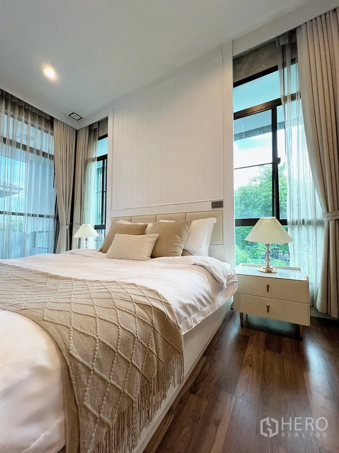 Detached House for rent in Prawet, Bangkok - Master bedroom with large bed, wood floors, and corner windows with full-length curtains.
