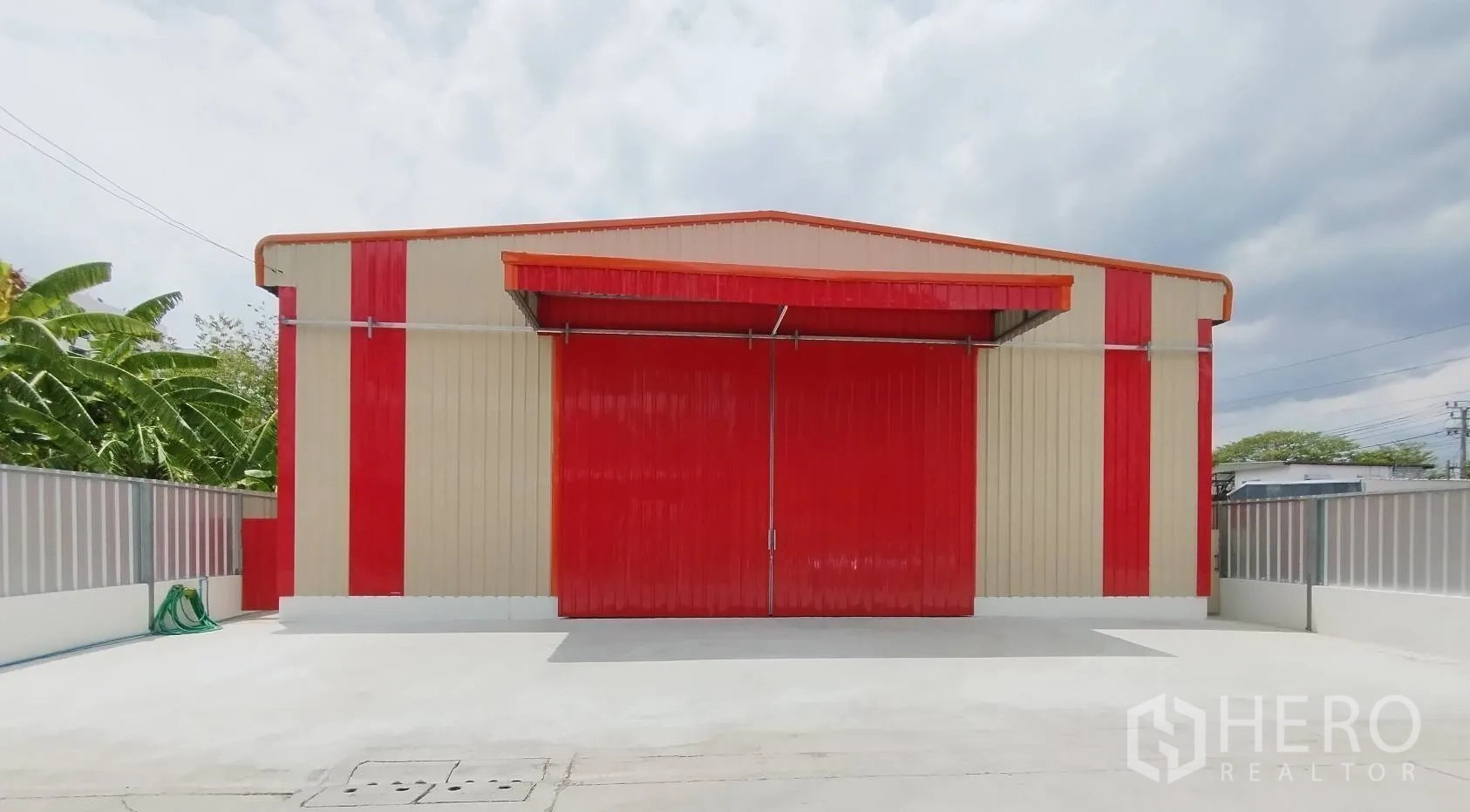 โกดัง for rent in Bang Khen, Bangkok - มุมมองหน้ากากอาคาร ประตูสีแดงปิดสนิท กรุผนังแดงครีม และรั้วล้อมรอบ