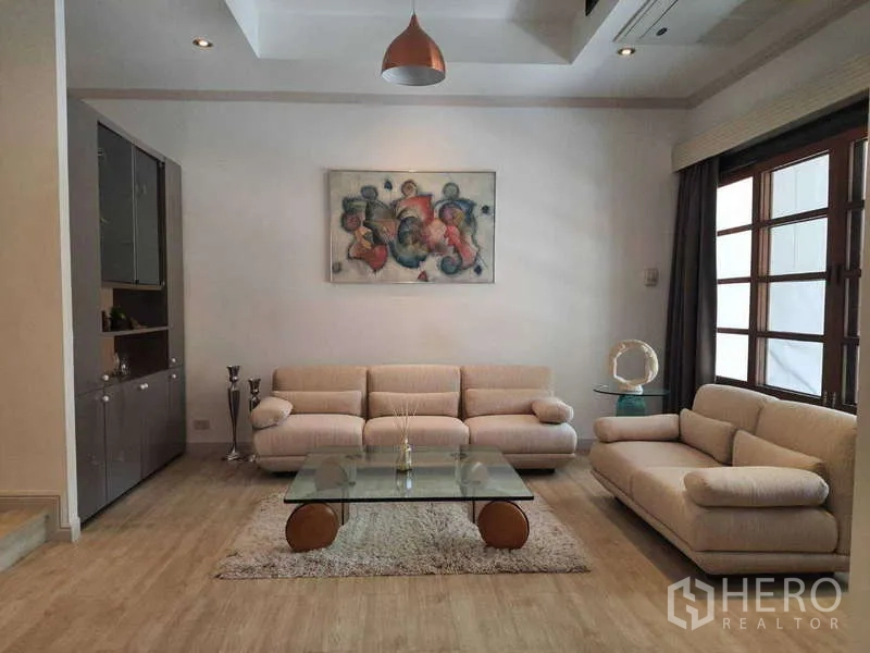 Townhouse for rent in Khlong Toei, Bangkok - Cozy lounge with beige sofas, glass coffee table and artwork.