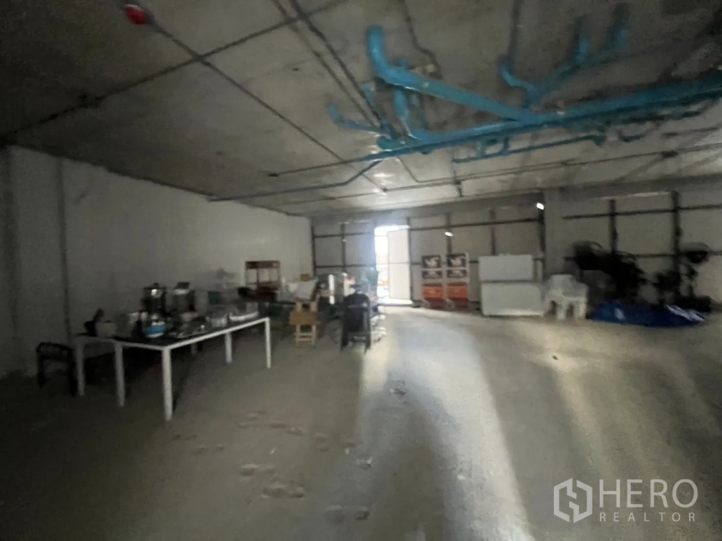 Retail Space for rent - Deep shop interior with natural light from a rear door and industrial ceiling piping.
