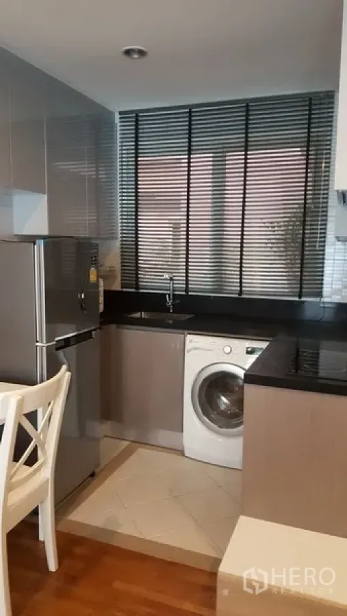 Condominium for rent in Watthana, Bangkok - Compact kitchen with black countertops, window blinds, stainless refrigerator, and a front-load washing machine.