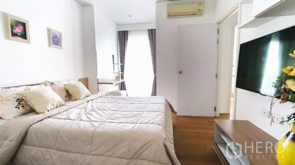 公寓 出租在Watthana, Bangkok - 主卧配大床、墙挂电视、木地板与带窗帘的阳台门。