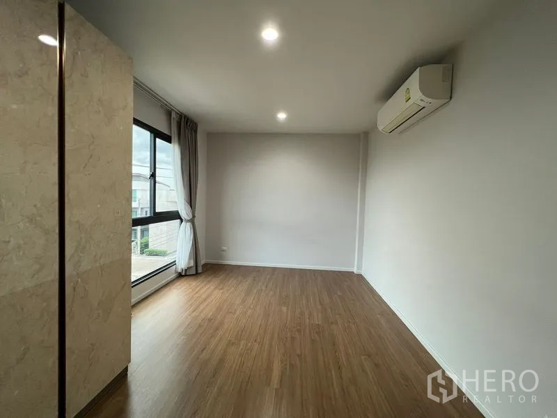 Detached House for rent in Saphan Sung, Bangkok - Bright bedroom with large window, split-type air conditioner and wood floors.