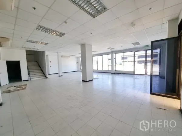 工厂 出租在Bang Pakong, Chachoengsao - 一层开放式办公/展示空间，设有楼梯与整面落地窗，地面为瓷砖。