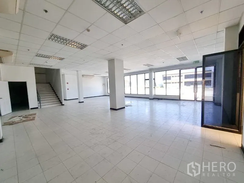工厂 出租在Bang Pakong, Chachoengsao - 一层开放式办公/展示空间，设有楼梯与整面落地窗，地面为瓷砖。