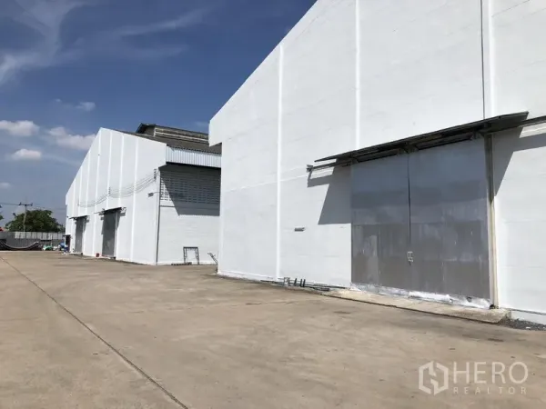 Warehouse for rent in Mueang Pathum Thani, Pathum Thani - Row of white warehouse blocks with wide concrete yard and large sliding steel doors in a secure compound.