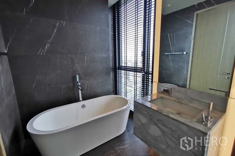 Condominium for rent or sale in Watthana, Bangkok - Bathroom with freestanding tub, marble vanity and city-view window blinds.