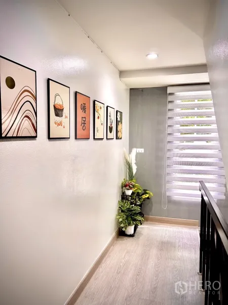 Townhouse for rent in Bang Kapi, Bangkok - Bright upstairs corridor with wall art, indoor plants and a window with roller blinds.