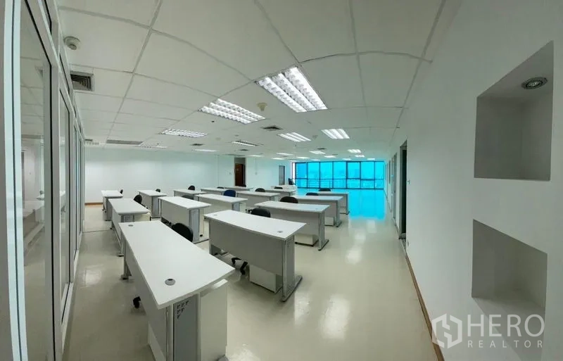 Office Space for rent - Open-plan office floor with rows of desks, bright lighting and glass partitions.