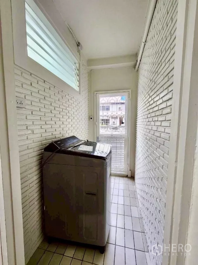 Townhouse for rent in Huai Khwang, Bangkok - Laundry area with top-loading washing machine, white painted brick walls and louvered window.