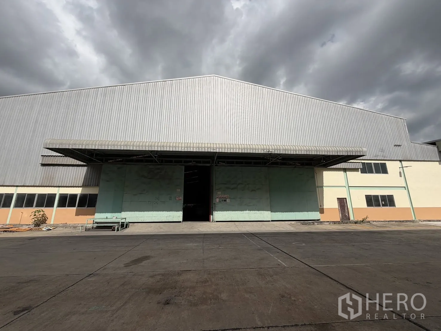 Factory for rent in Bang Na, Bangkok - Exterior of metal-clad factory with large sliding doors, a covered loading bay, and a wide paved yard.