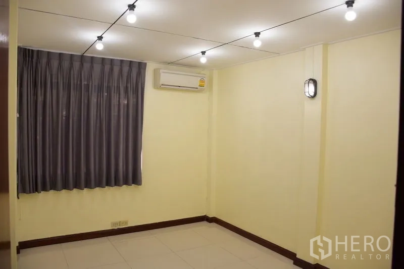 Townhouse for rent in Watthana, Bangkok - Empty room with grey curtains, split AC and string ceiling lights.
