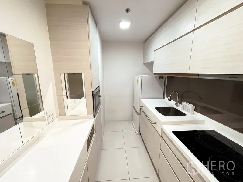 Condominium for sale - Compact galley kitchen with white cabinetry, sink, electric cooktop and refrigerator.