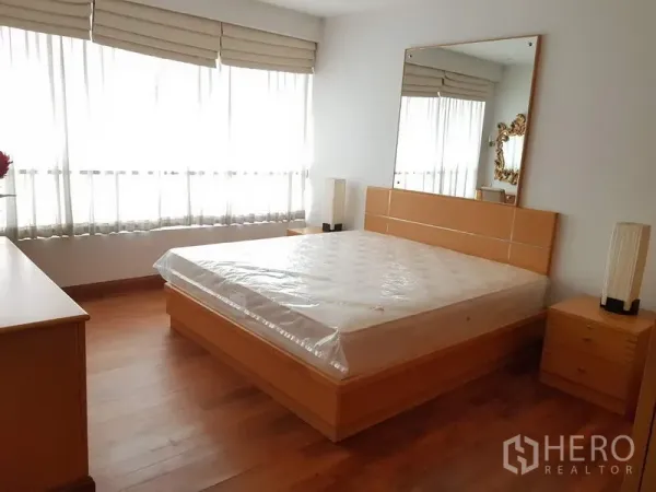 Condominium for rent in Pathum Wan, Bangkok - Master bedroom with large windows, queen bed, mirror headboard and warm wood flooring.