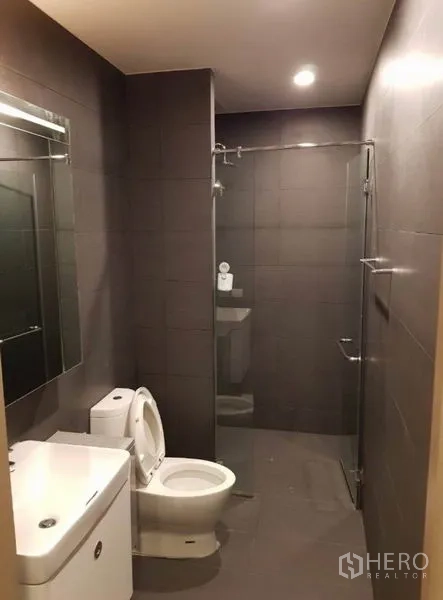 Condominium for rent in Pathum Wan, Bangkok - Spacious bathroom with walk-in glass shower, large mirror and gray tiles.