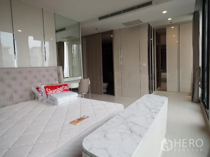 คอนโด ให้เช่าในPathum Wan, Bangkok - ห้องนอนพร้อมเตียงบุนวม ม้านั่งท็อปหินอ่อน โต๊ะเครื่องแป้ง และทางเข้าห้องน้ำ