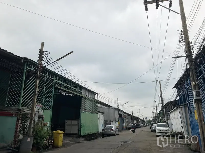 货栈 出租在Bang Phli, Samut Prakan - 工业区道路外景，成排金属仓库与车辆通行，架空电线分布于邦帕里一带。