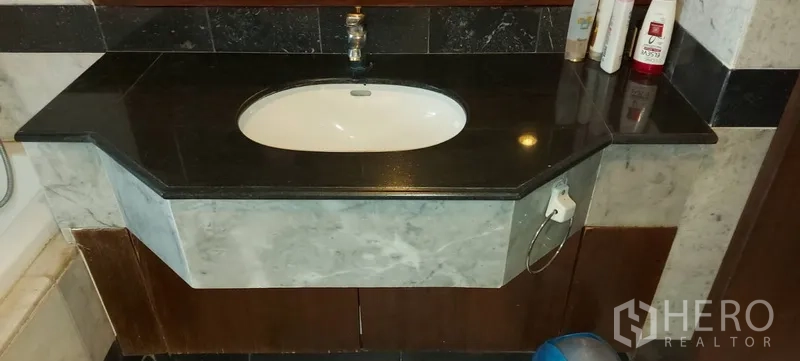 Condominium for rent in Sathon, Bangkok - Bathroom vanity with black granite countertop and under-sink cabinet.