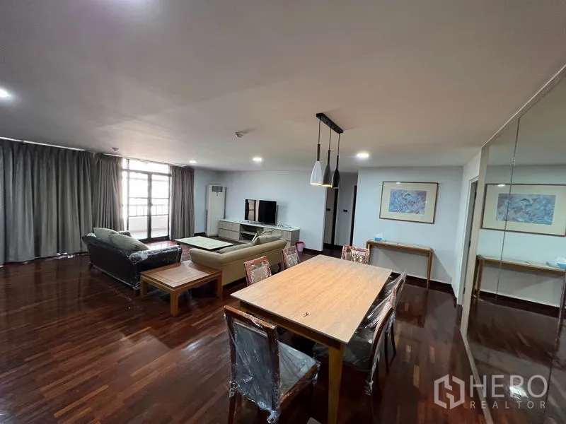 Condominium for rent or sale in Watthana, Bangkok - Open-plan lounge and dining room with long wooden table, large windows and TV area.