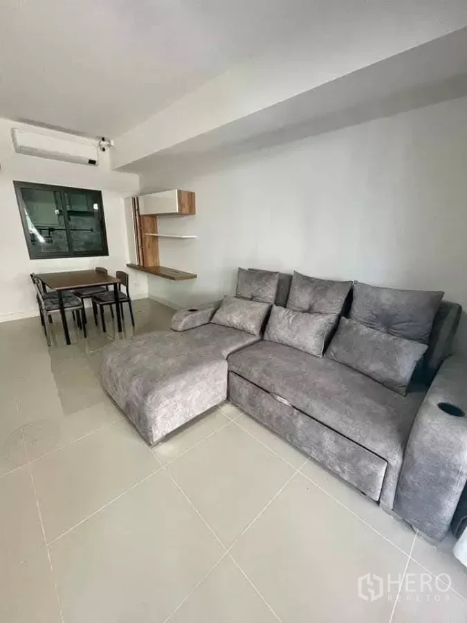 联排别墅 出租在Bang Phli, Samut Prakan - 明亮客厅，灰色转角沙发、瓷砖地面、餐桌与墙面层架