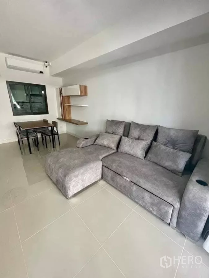 联排别墅 出租在Bang Phli, Samut Prakan - 明亮客厅，灰色转角沙发、瓷砖地面、餐桌与墙面层架