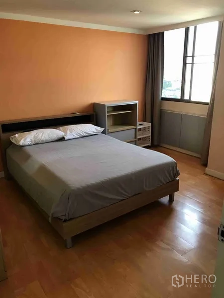 Condominium for rent or sale in Watthana, Bangkok - Cozy second bedroom with peach accent wall, double bed and storage beside the window.