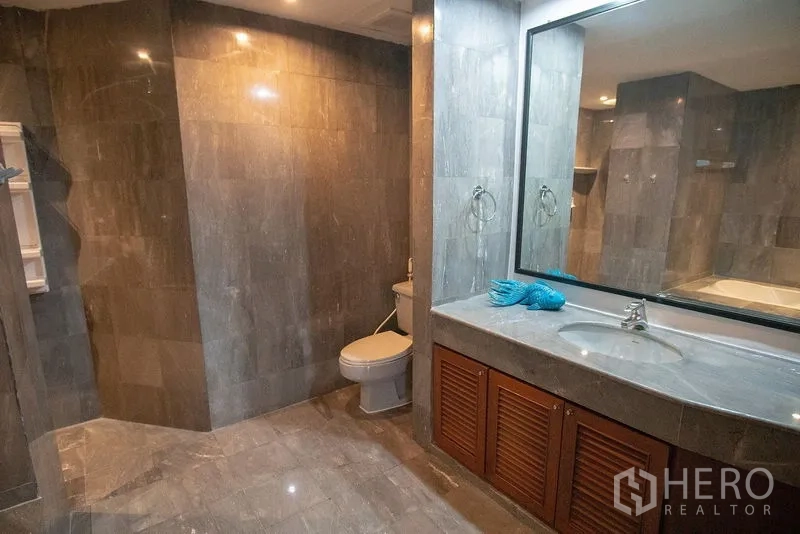 Apartment for rent in Watthana, Bangkok - Bathroom vanity with large mirror, storage cabinets and toilet finished in stone tiles.